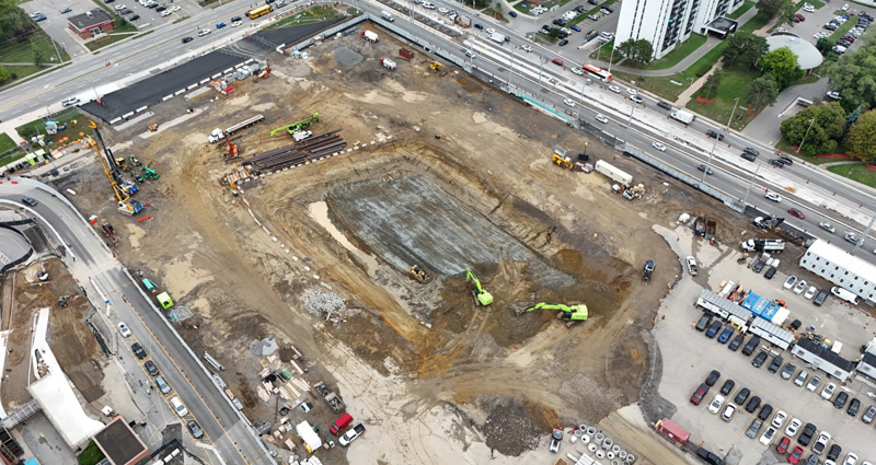 A construction site with cranes, heavy equipment, and a city skyline in the background.